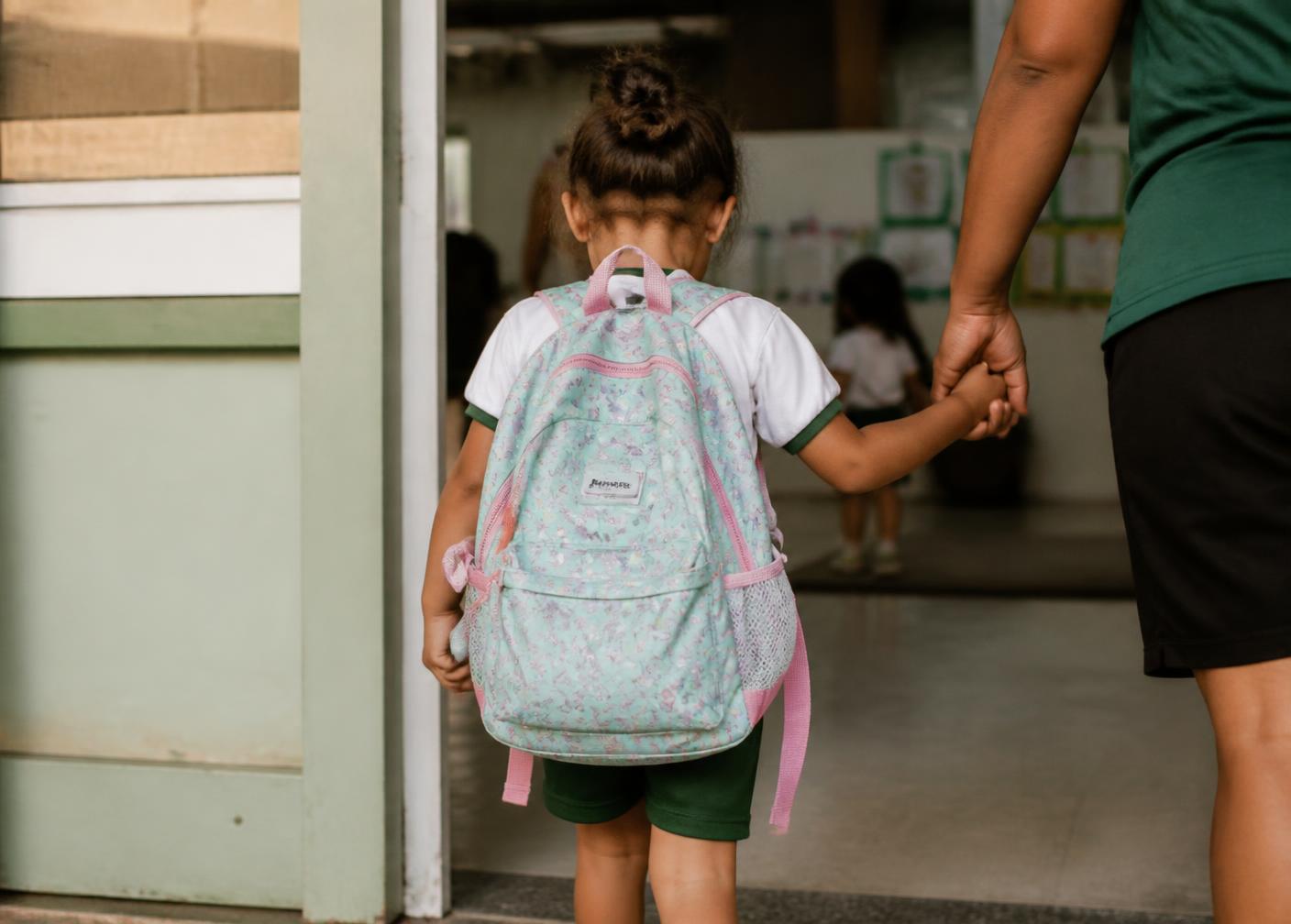 Criança com mochila entrando na creche de mãos dadas com um adulto